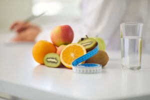 Fruits with glass of water and measuring tape on white table, symbolizing health.