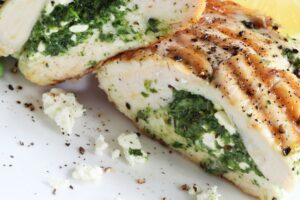 Stuffed chicken breast with green filling and crumbled cheese on a white plate
